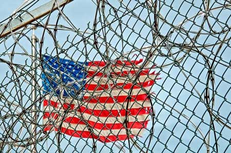 U.S. flag flies behind razor wired fence.